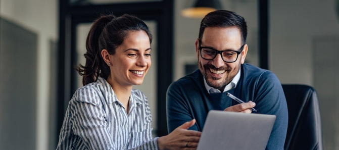 Two friends smiling while using embedded finance platform on laptop