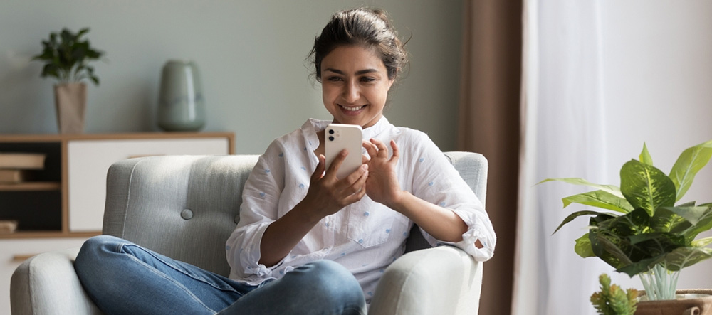 Woman sitting on couch and managing personal finances on app.