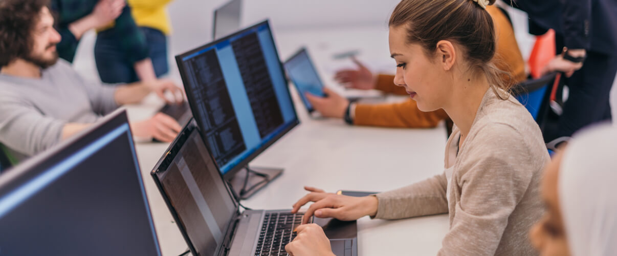 Female nearshore developer working on computer with other nearshore developers.