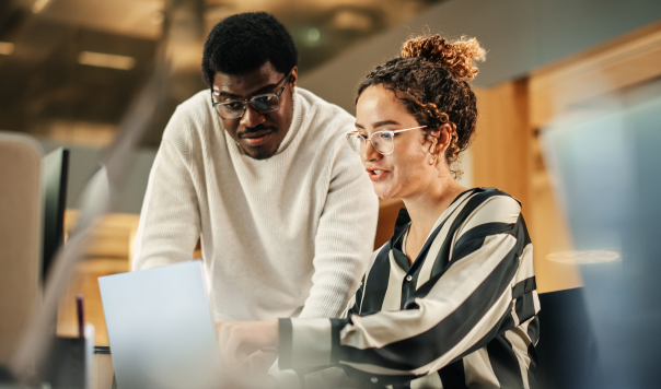 Two developers looking at a laptop and looking through the top software development outsourcing trends.
