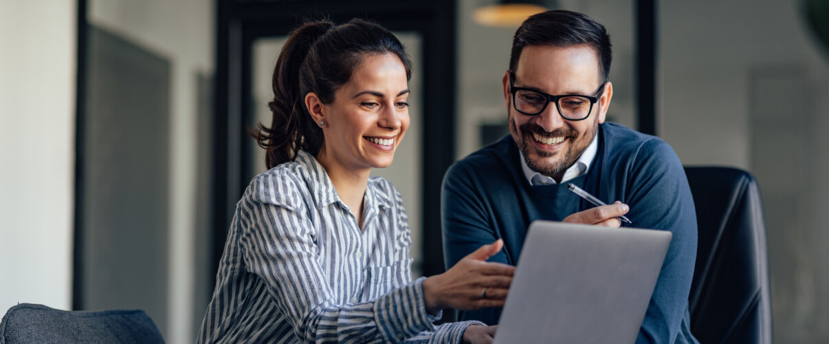 Two nearshore developers smiling while collaborating on one computer.